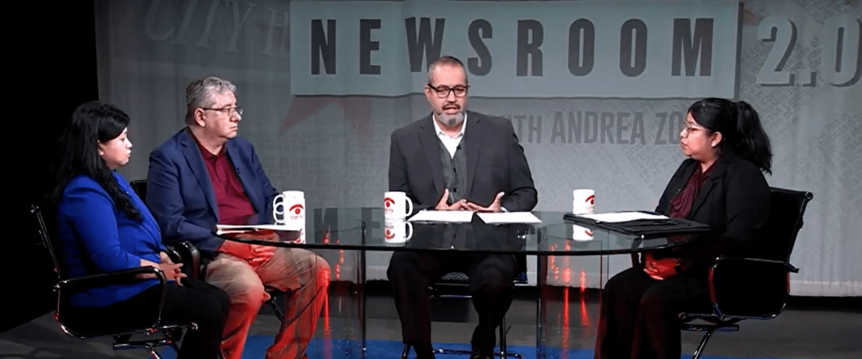3 individuals sitting around a table in a newsroom.